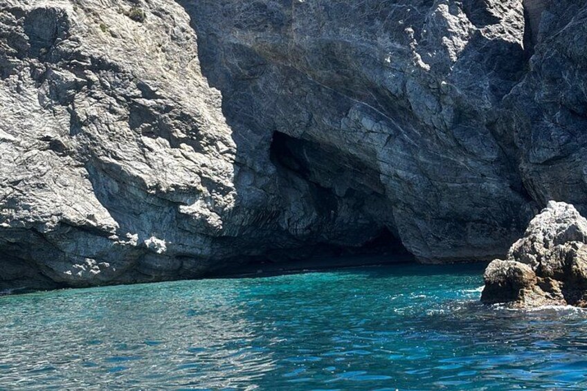 A rocky coastline with clear turquoise water and a cave entrance. 3