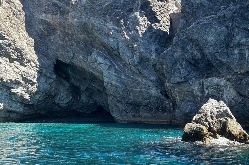 A rocky coastline with a cave entrance and clear turquoise water. 1
