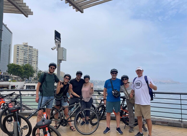 Un grupo de personas con bicicletas junto a la costa, con edificios y un cielo despejado al fondo. 5