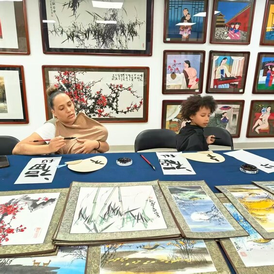 Two people seated at a table with traditional Chinese calligraphy and paintings. 3