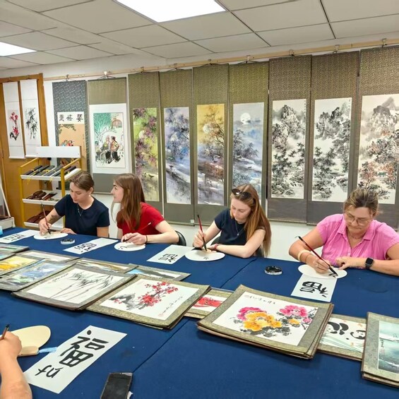 A group of people engaged in a calligraphy class, with traditional Chinese paintings in the background. 2