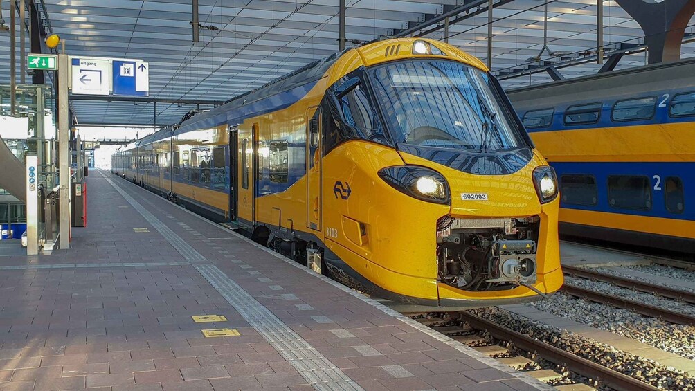 A yellow train at a station platform with overhead signs and tracks. 2