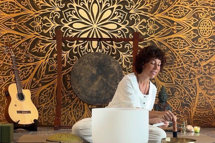 A person sitting on the floor with a laptop, surrounded by a decorative wall with intricate patterns, a guitar, and a small statue. 2