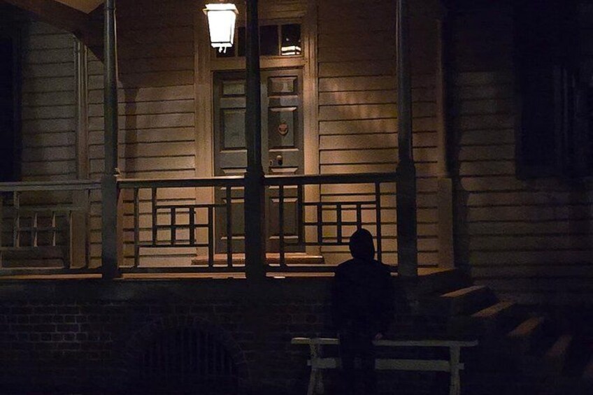 A wooden building with a porch, a person sitting on a bench, and a street lamp. 4