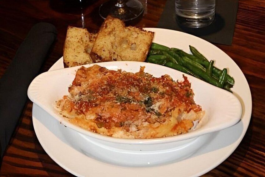 A dish of baked pasta with a golden-brown crust, accompanied by green beans and toasted bread on a white plate. 2