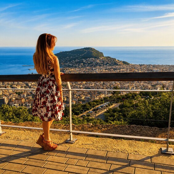 A person standing on a balcony overlooking a coastal cityscape with a hill in the distance. 3