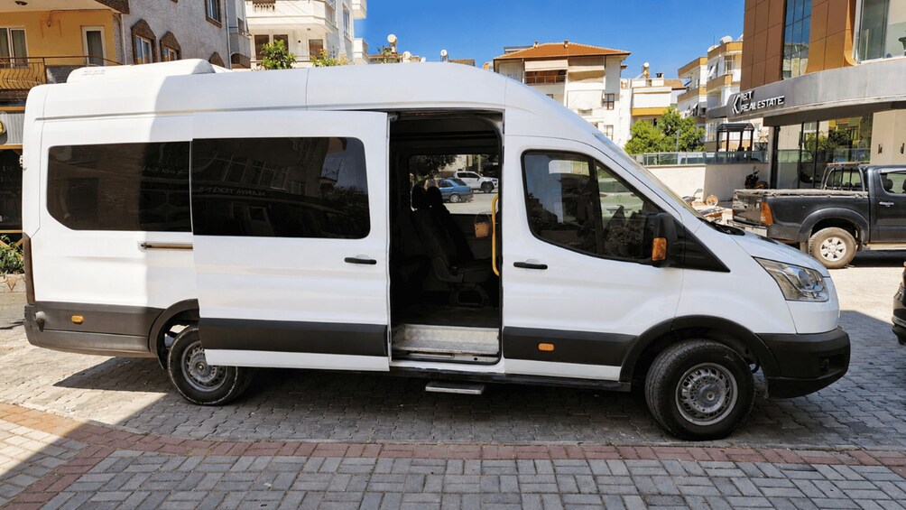 A white van parked on a paved street with buildings in the background. 2