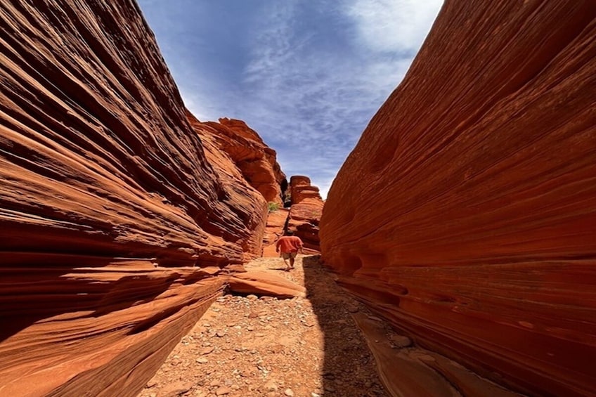 A narrow canyon with red rock walls and a person walking down the trail. 1