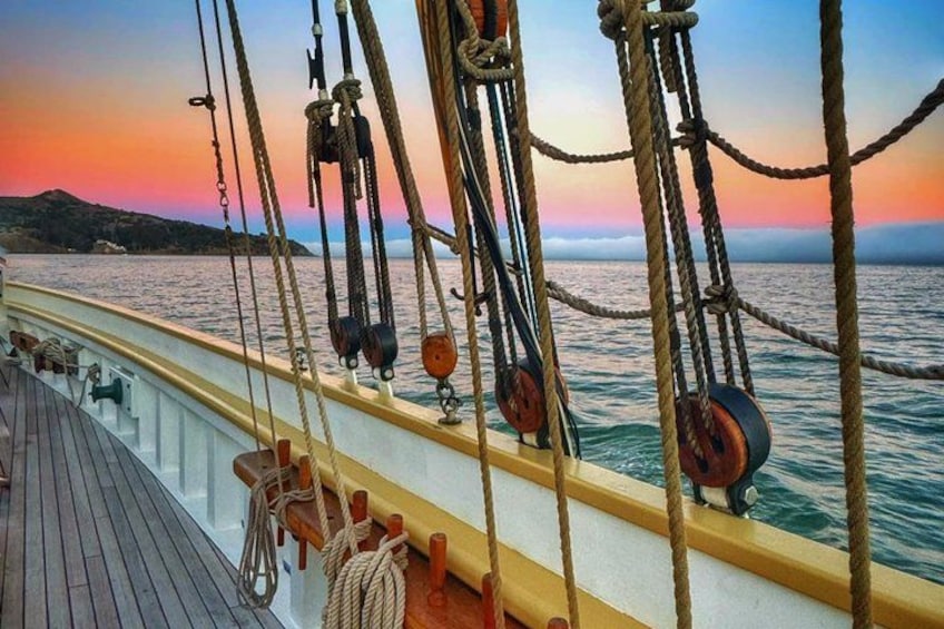 A ship's deck with ropes and pulleys, a wooden floor, and a sunset over the water. 4