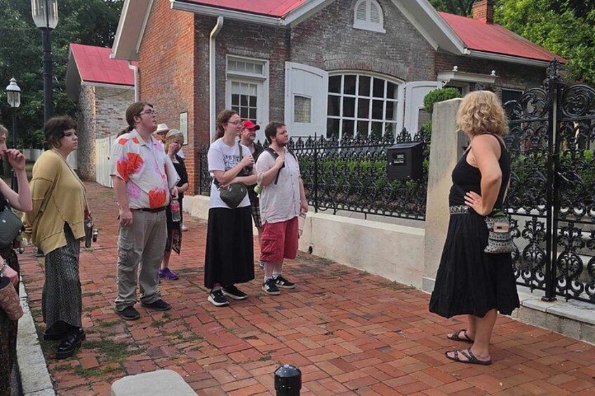 A group of people standing on a brick pathway in front of a brick building with a red roof. 4