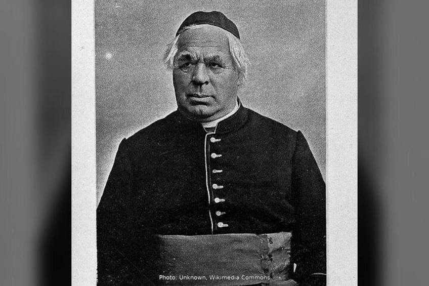 A person in a formal, dark robe with a white collar and cuffs, holding a book or document. 4
