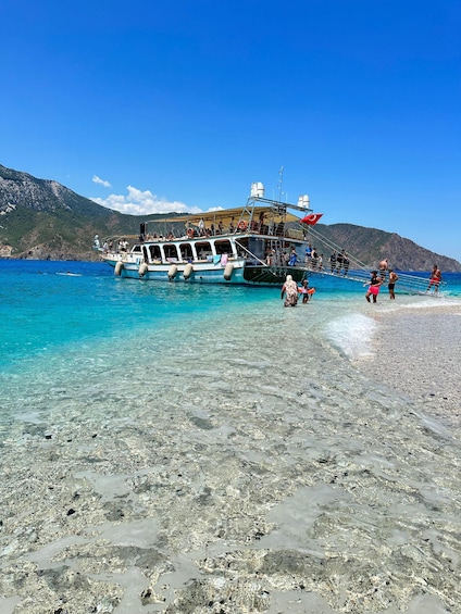 A boat with passengers disembarking onto a clear, rocky beach with mountains in the background. 3