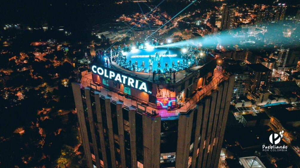 A nighttime aerial view of a building with 'COLPATRIA' illuminated on its facade. 2