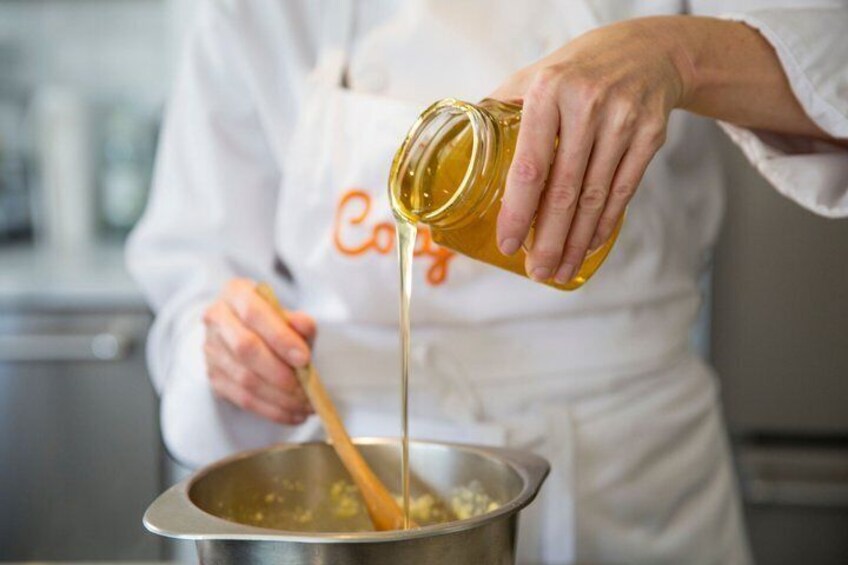 A person pouring a yellow liquid from a jar into a pot with a wooden spoon. 2