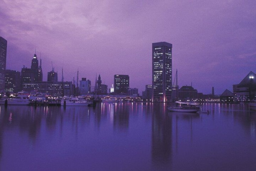 A city skyline at dusk with illuminated buildings and a calm waterfront. 1
