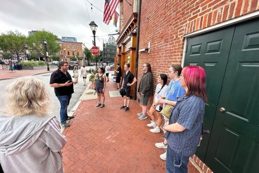 A group of people standing on a brick sidewalk, a brick building, and a stop sign. 2