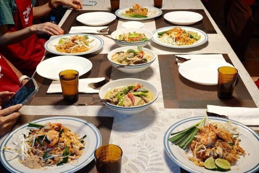 A table with various dishes, including noodles and seafood, and people sitting around it. 1