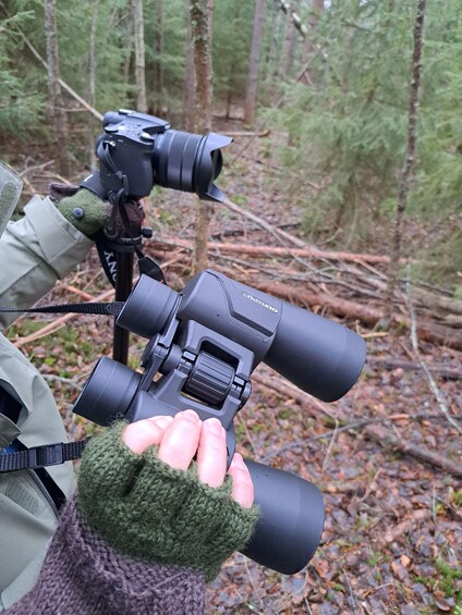 A person holding a binoculars with a strap and a green glove. 4