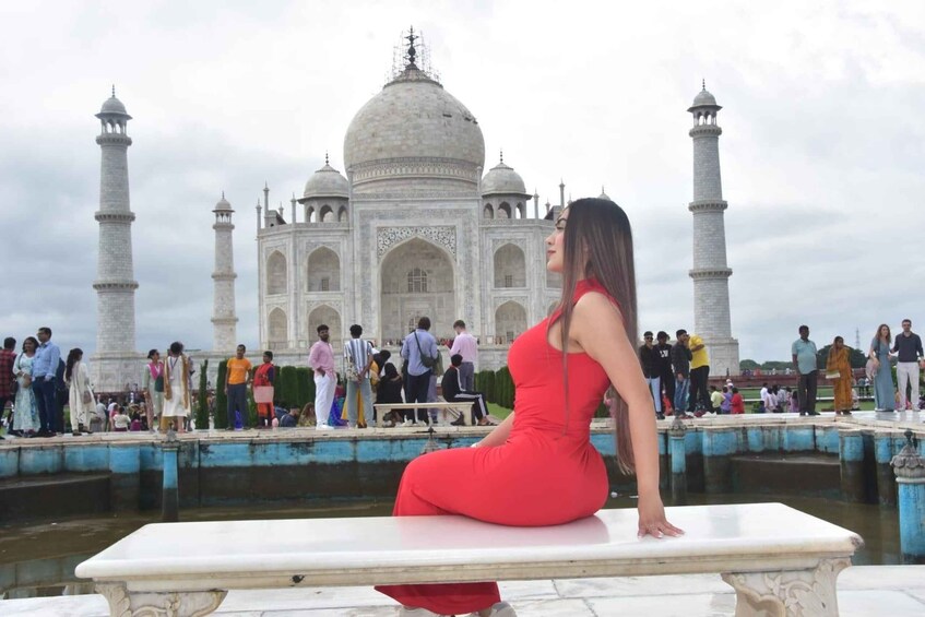 A woman in a red dress sitting on a marble bench with the Taj Mahal in the background. 2