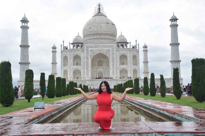 A person in a red dress standing in front of the Taj Mahal with arms outstretched. 3