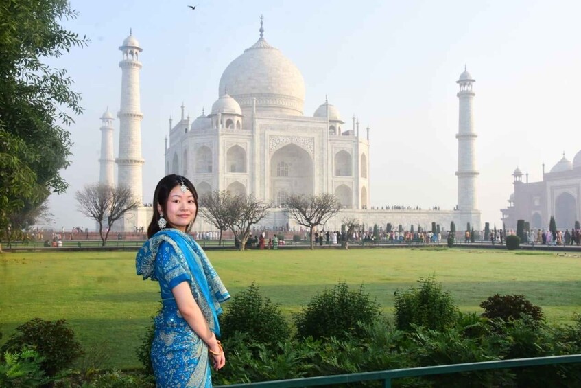 A person in a blue dress standing in front of the Taj Mahal with its four minarets and large dome. 1
