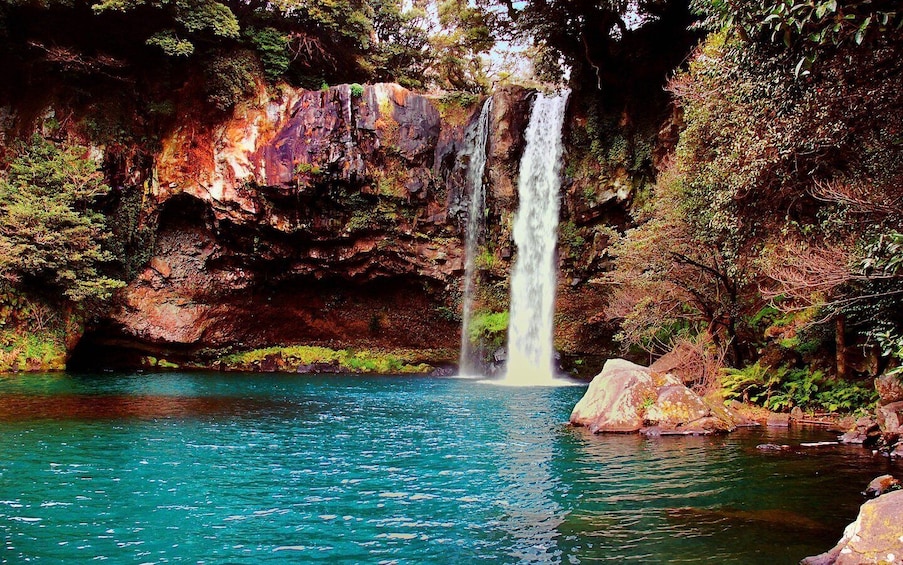 A waterfall cascading into a clear blue pool surrounded by rocky cliffs and lush greenery. 3