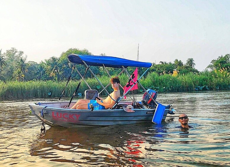 A boat with a blue canopy and the word 'LUCKY' on its side, floating on water with a person in the front and another person in the water behind it. 2