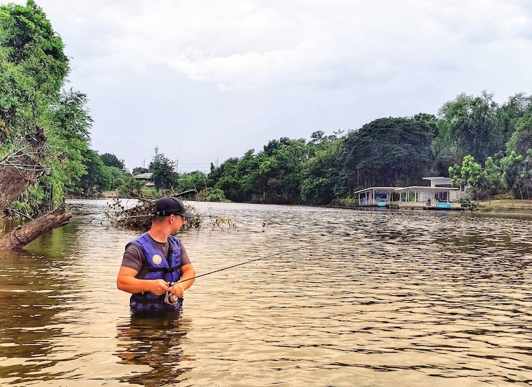 A person fishing in a river with a houseboat in the background. 5