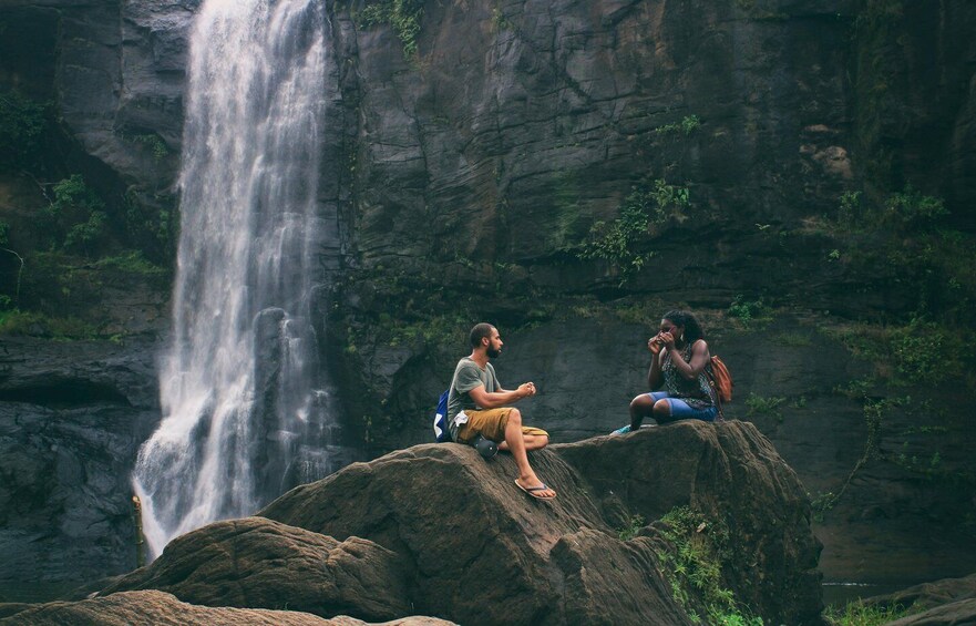 Dos personas sentadas sobre una roca junto a una cascada. 1