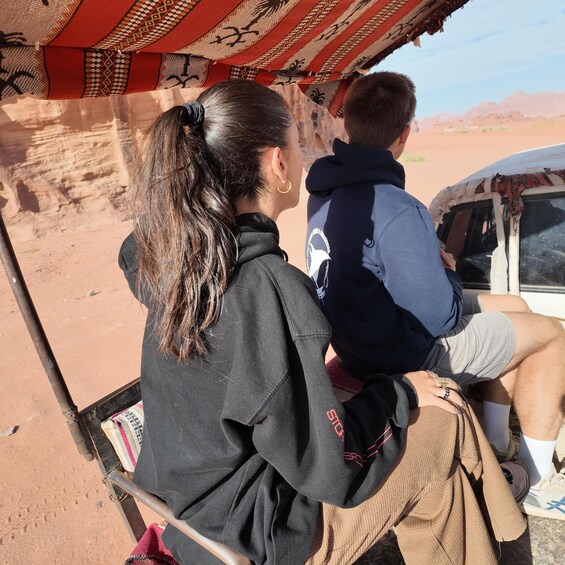 Two people seated in a vehicle with a desert landscape in the background. 4
