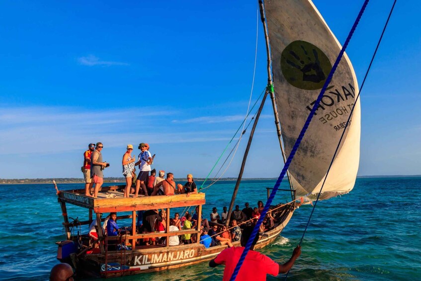 A traditional sailing boat with passengers, named 'KILIMANJARO,' on a clear day. 1