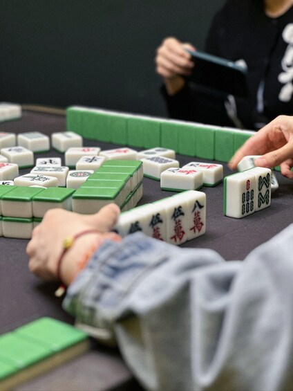A person playing a tile-based game, likely Mahjong, with tiles arranged on a table. 1