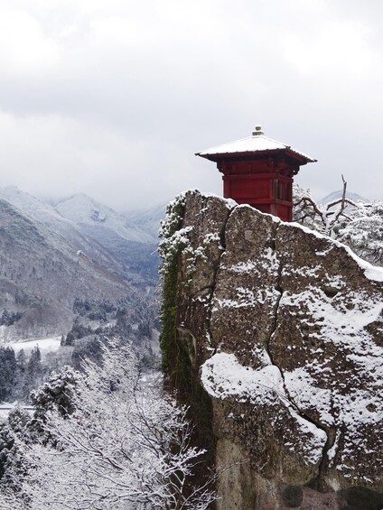 A red pagoda on a snow-covered rock with a mountainous backdrop. 3