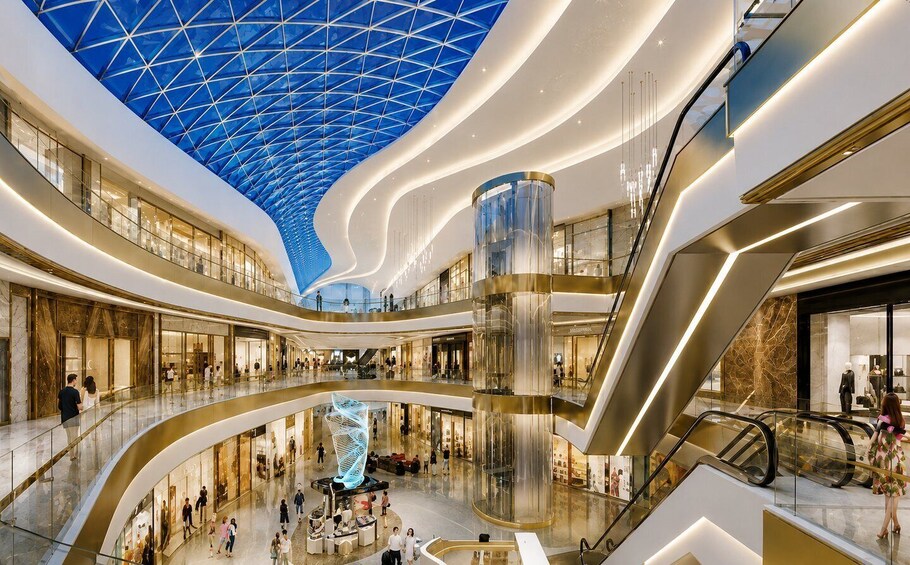 A modern shopping mall with a distinctive blue glass ceiling, multiple levels, and a central spiral sculpture. 3