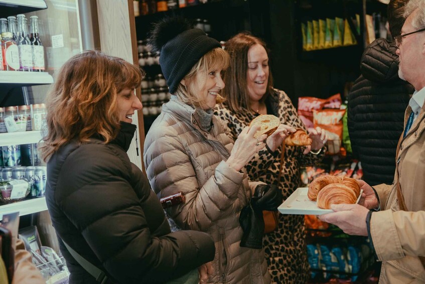 People in a store, one holding a plate with croissants. 1