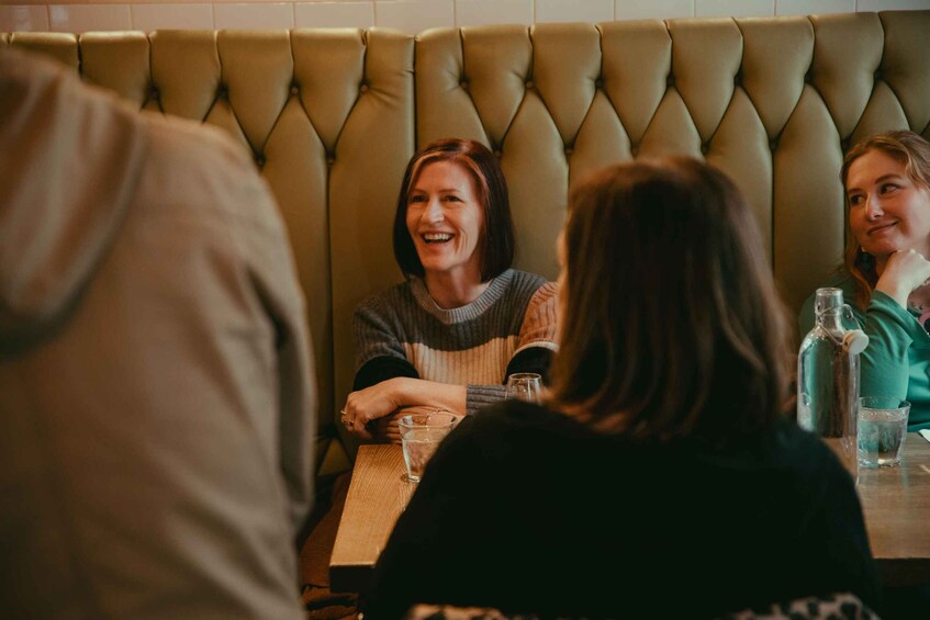 A group of people seated at a table in a restaurant with a tufted leather booth in the background. 5