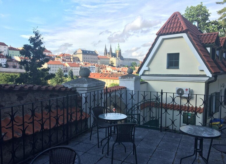 A terrace with two round tables and chairs, overlooking a cityscape with historic buildings and a church spire. 3