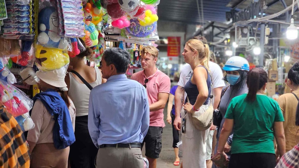 People shopping in a market with colorful balloons and various items on display. 1
