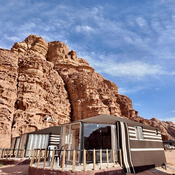 A desert landscape with a large rock formation and a caravan parked in front of a glass-walled structure. 3