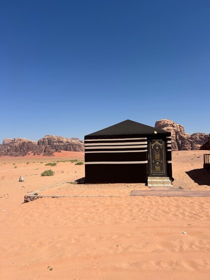 A small, black tent-like structure with a decorative door in a desert landscape with red rock formations in the background. 5