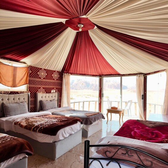 A bedroom with a large bed, two smaller beds, a wooden chair, and a view of a desert landscape through large windows. 2
