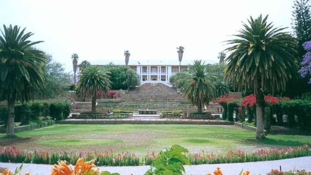 A formal garden with a central staircase, palm trees, and a building with columns. 2