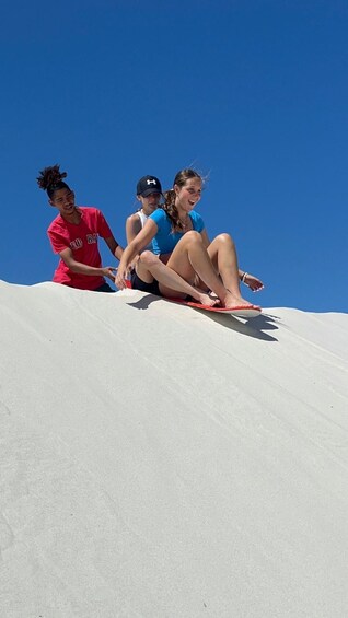 Three people sitting on a sand dune with a clear blue sky. 5