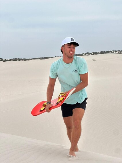 A person walking on a sandy beach holding a red paddleboard. 4