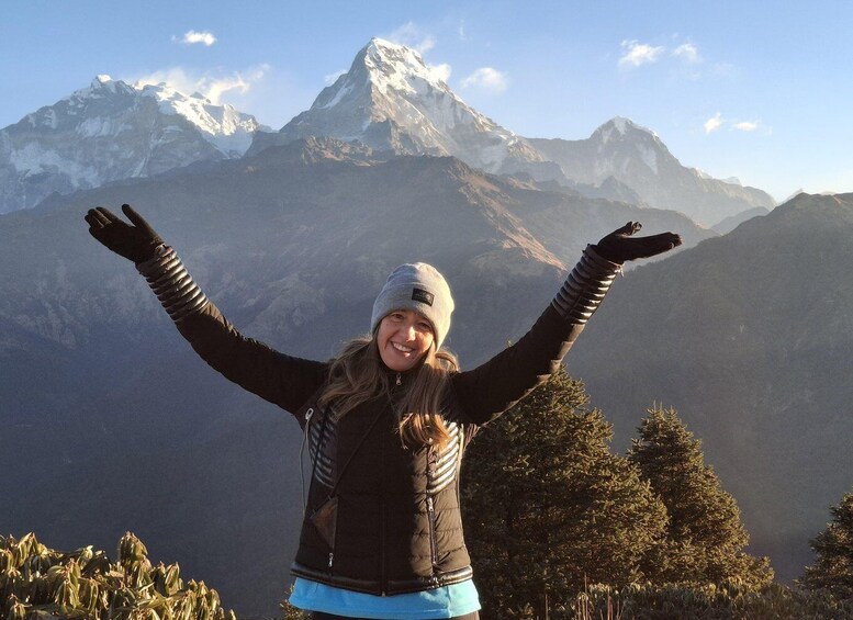 A person standing with arms raised, wearing a jacket and a beanie, with a mountainous landscape in the background. 3