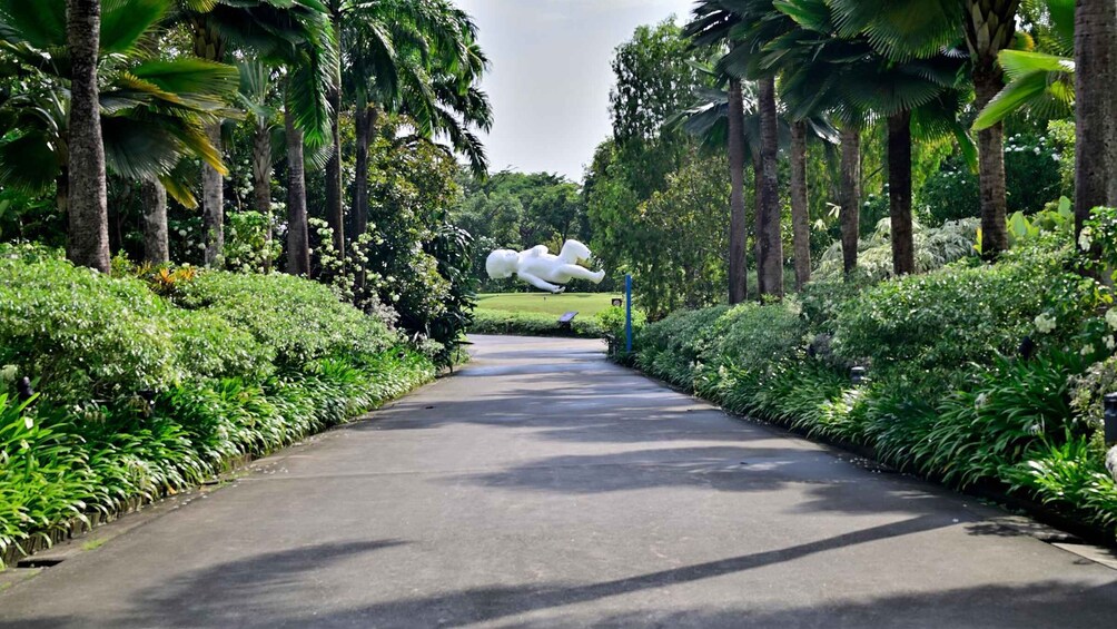 A pathway flanked by lush greenery and palm trees, leading to a white sculpture of a figure in a dynamic pose. 4