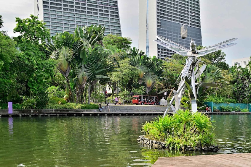 A park with a dragonfly sculpture, a pond, and tall buildings in the background. 2