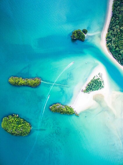 An aerial view of a turquoise sea with several small islands, a clear demarcation line, and a sandy beach. 2