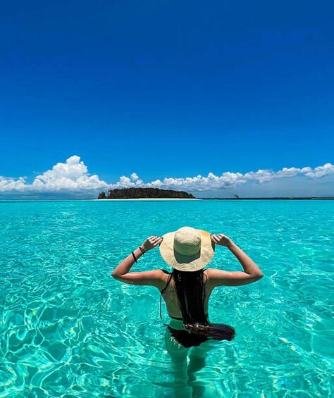 A person in clear turquoise water, wearing a hat, with a distant island and a clear blue sky. 5