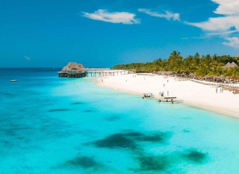 A beach with clear turquoise water, a white sandy shore, a thatched-roof structure, and a pier extending into the water. 4